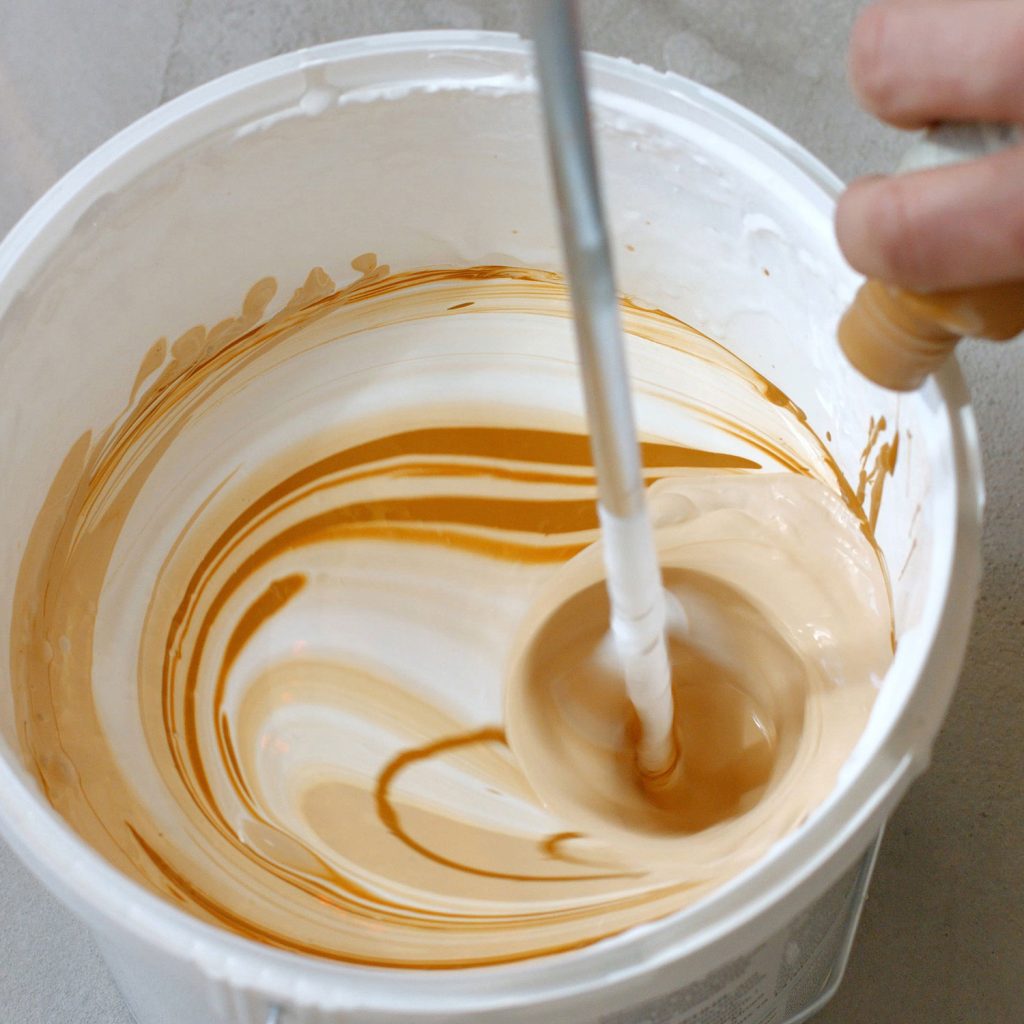 hand-pouring-brown-liquid-into-white-paint-2023-11-27-05-23-18-utc